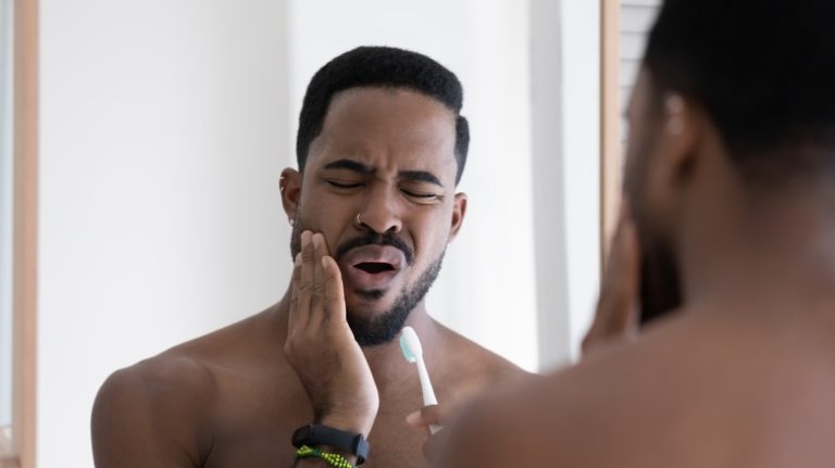 The Surprising Impact of Stress on Your Gum Health man touching cheek and brushing teeth